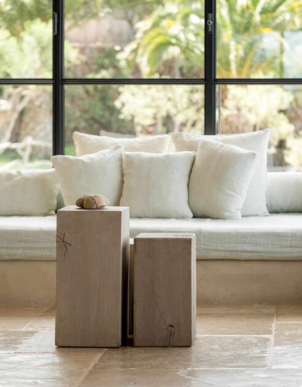 Interior luminoso con suelos de piedra natural, mesas rústicas de madera y grandes ventanales con vistas a un frondoso jardín.